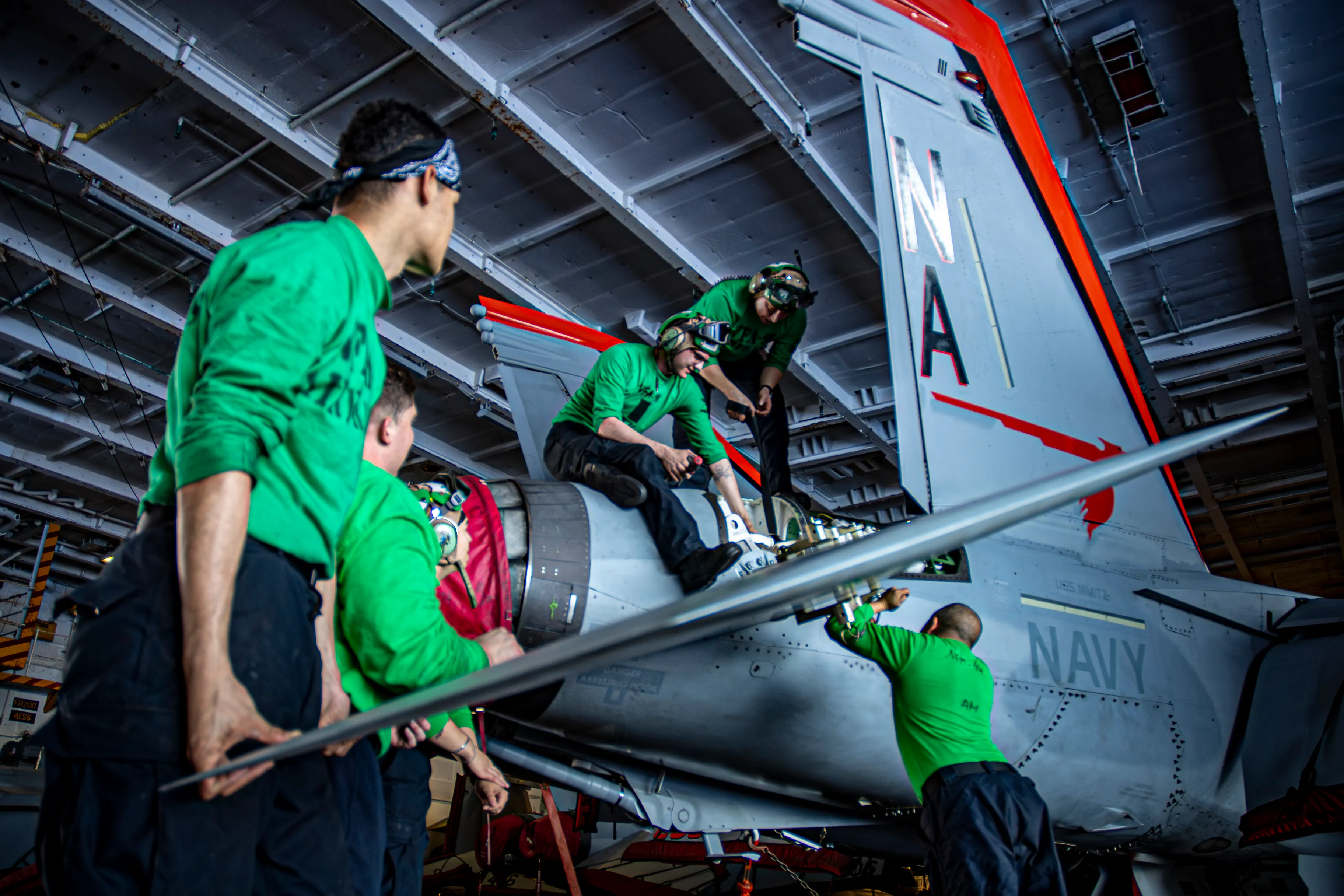 Sailors perform maintenance on an F/A-18E Super Hornet in the USS Nimitz hangar bay.